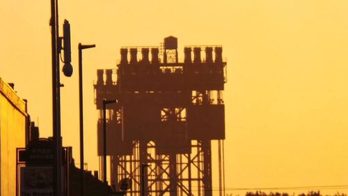 Cranes in city against sky during sunset