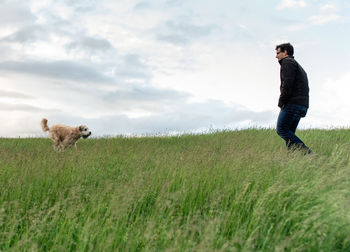 Dog running to it's male owner through a tall grassy field.