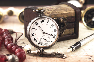 Close-up of pocket watch with box and pen on table