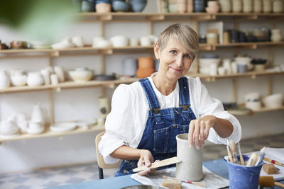 Portrait of smiling mature woman with earthenware at table in art studio