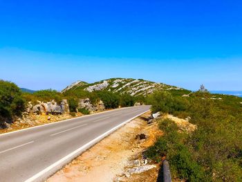 Road leading towards mountain against blue sky