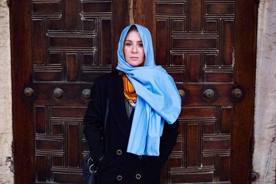 Portrait of young woman standing against door