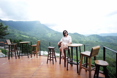 Young woman sitting on chair at table against mountains