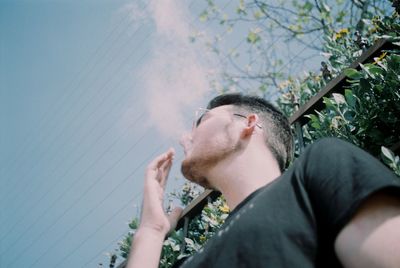 Low angle view of young man smoking against sky