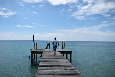 Rear view of man running on pier over sea against sky