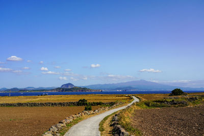 Empty road amidst field against sky