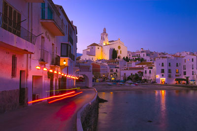 Illuminated buildings by road against sky at dusk