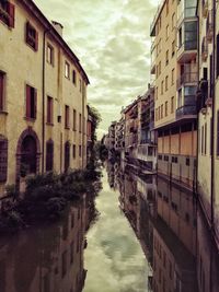 Canal amidst buildings in city against sky