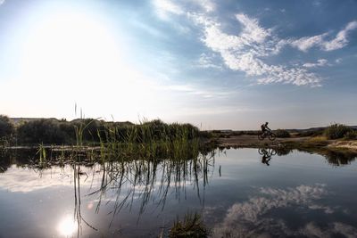 Man cycling by lake against sky