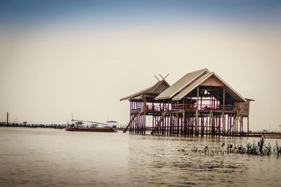 Stilt house in sea against clear sky