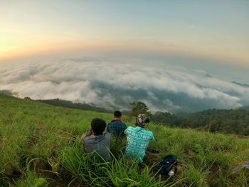 Rear view of men sitting on field against sky