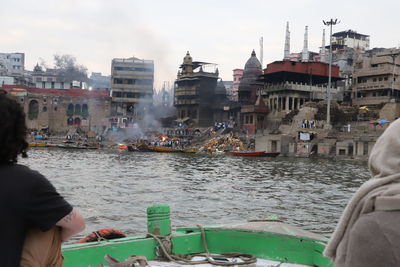 People on river by buildings in city against sky