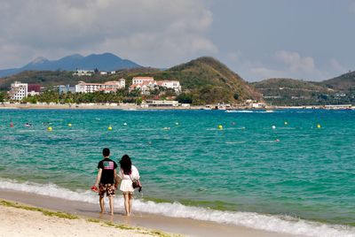 Rear view of men on beach against sky