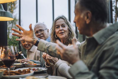 Senior woman listening to male friend gesturing while talking at dinner party