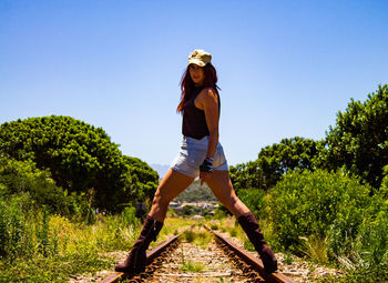 Full length of young woman standing against plants on a railroad track 