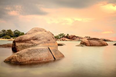 Rocks in sea against cloudy sky during sunset