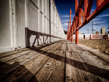 Wooden walkway by wall against sky