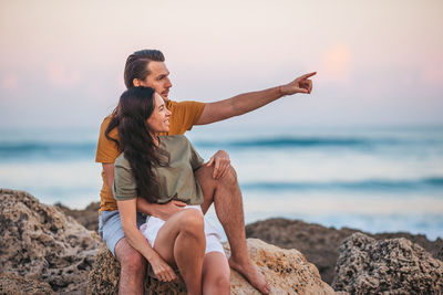 Young woman exercising at beach against sky during sunset