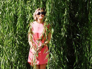 Young woman wearing sunglasses standing against willow tree