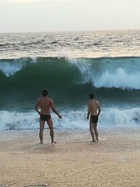 Rear view of shirtless men on beach against sky