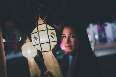 Portrait of smiling woman holding lantern at night