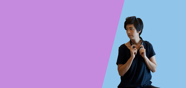 Young woman looking away while standing against pink wall