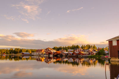 Houses by lake against sky during sunset