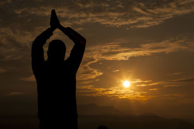 Silhouette man praying against sky during sunset