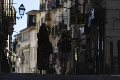 Rear view of women walking on street amidst buildings