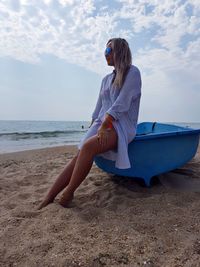 Woman sitting on bathtub at beach against sky