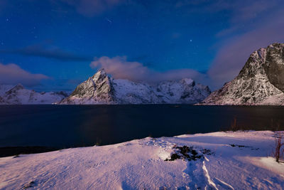 Scenic view of lake by snowcapped mountains against sky at night