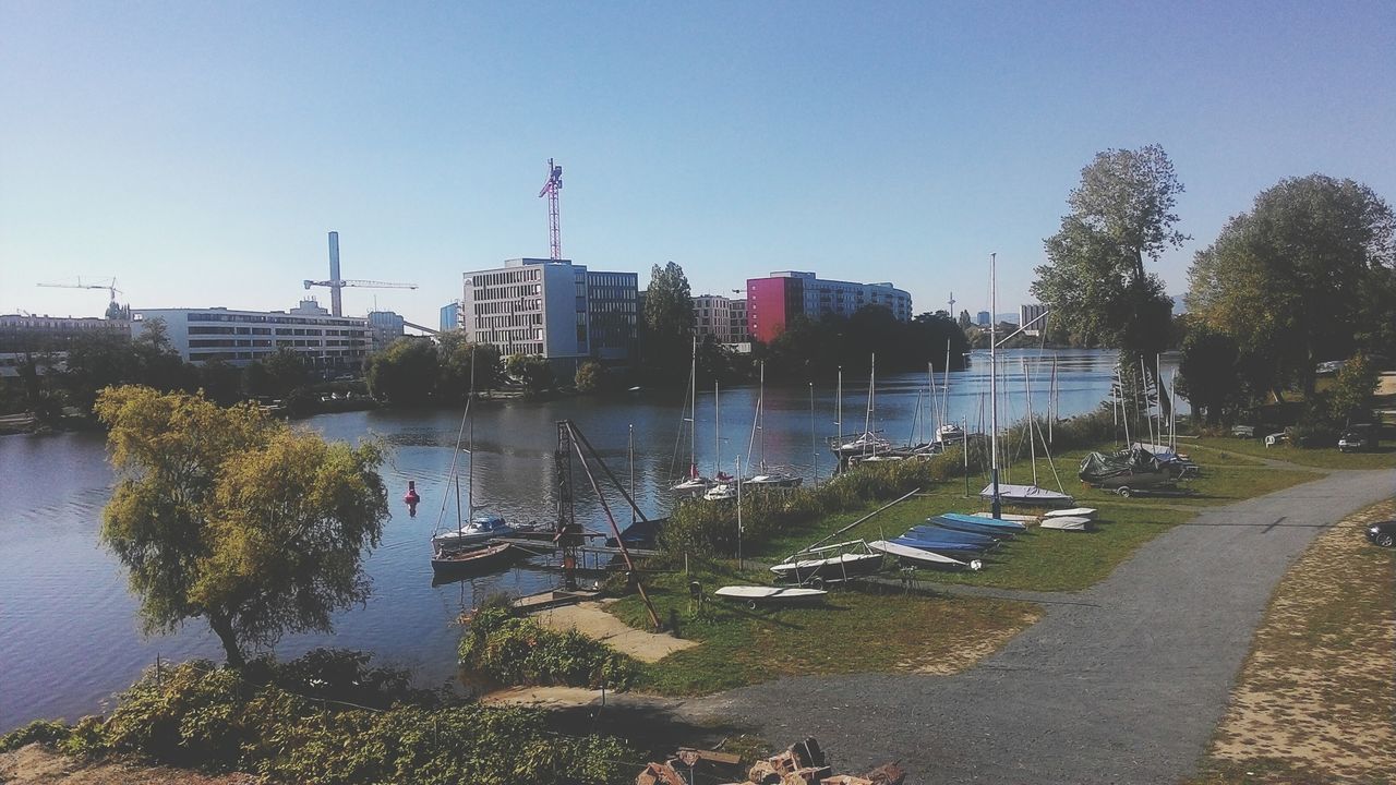 clear sky, water, building exterior, built structure, copy space, architecture, tree, river, blue, city, lake, transportation, day, sunlight, sky, nature, outdoors, nautical vessel, moored, tranquility