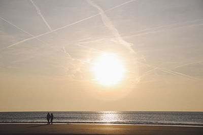 People standing at sea shore against sky during sunset