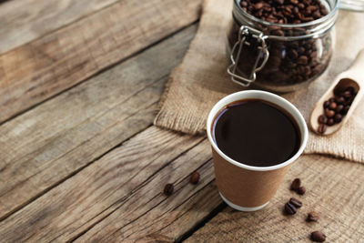 Paper cup of black coffee espresso, dry roasted coffee beans in jar at old wooden table