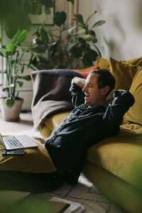 Male entrepreneur yawning with hands behind head in living room at home