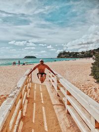 Rear view of shirtless man on beach against sky