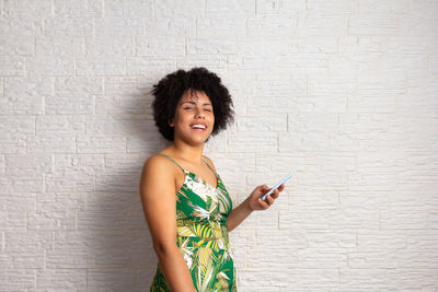 Portrait of young black woman using mobile phone against wall