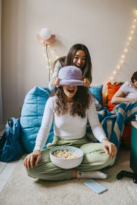 Happy young woman covering eyes of friend at home