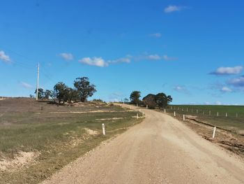 Dirt road amidst field against blue sky