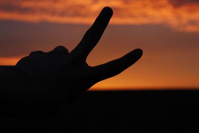 Close-up of silhouette hand against sky during sunset
