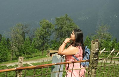 Side view of woman standing by railing against trees