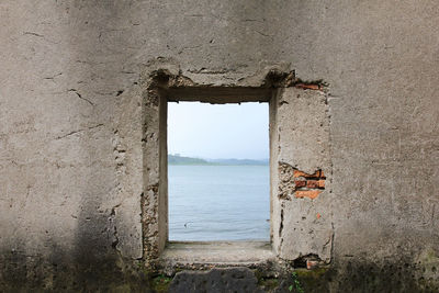 Window of old building by sea against sky