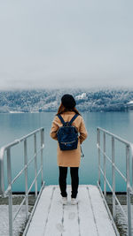 Rear view of backpack woman standing by lake during winter
