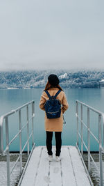 Rear view of man standing on railing against sea