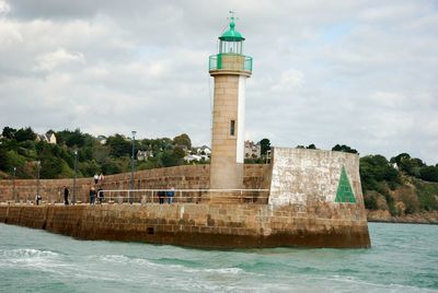 Lighthouse on building by sea against sky