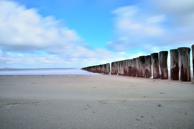 Wooden post at beach against blue sky