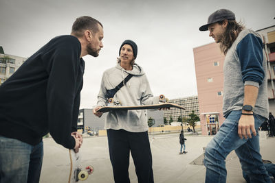 Man talking with male friend while holding skateboard at park