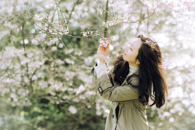 Side view of young woman standing against tree