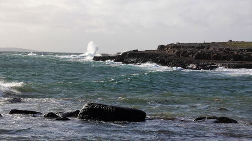 Sea waves splashing on rocks against sky