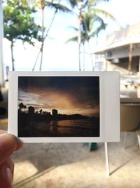 Close-up of person holding camera against sky